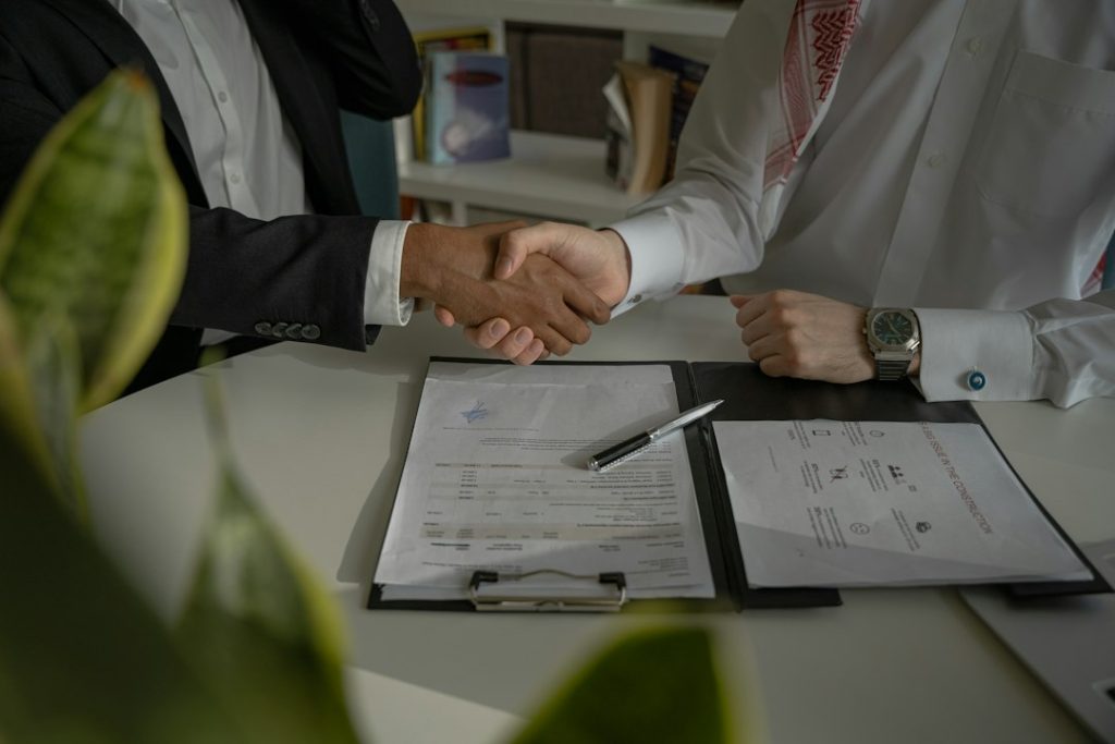 Poignée de main au-dessus d’un dossier ouvert et de documents sur une table, avec une personne portant un gilet de travail