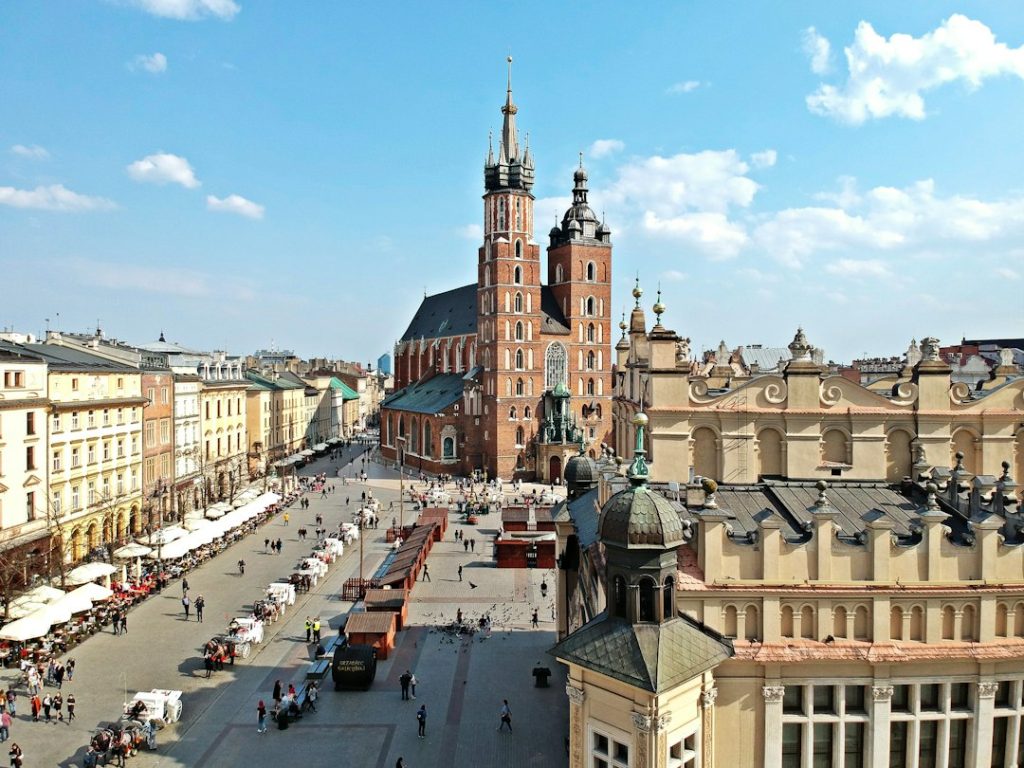 Place urbaine bordée de façades historiques, avec une église à deux tours et des terrasses au premier plan