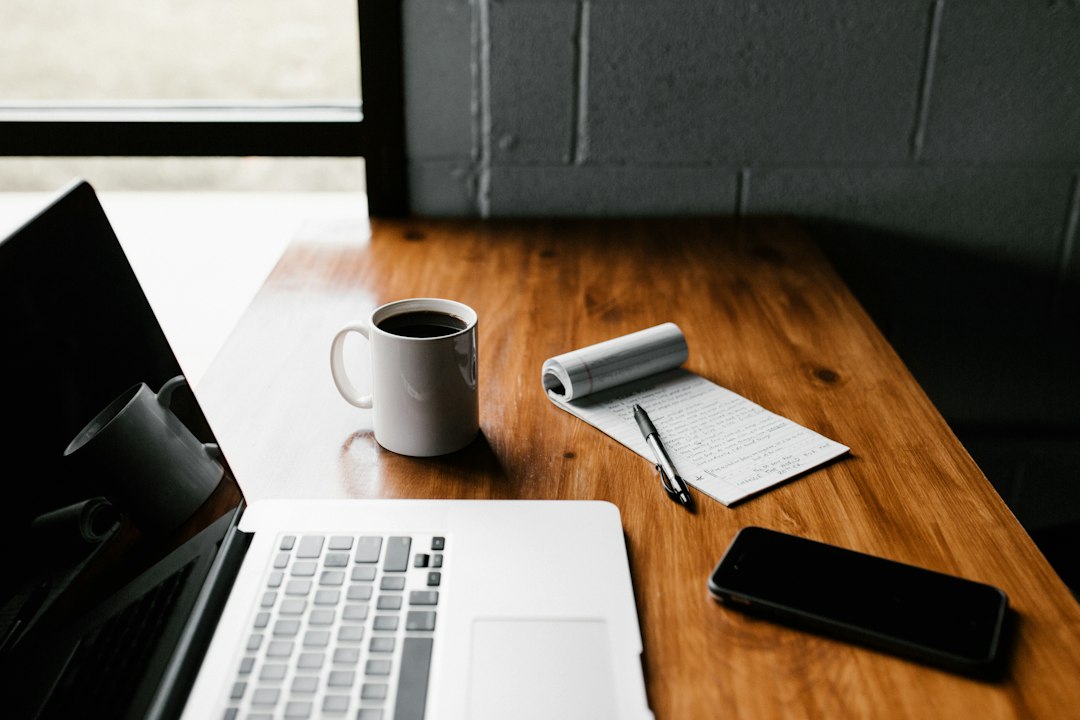 Préparer les documents de création de société en Pologne Ordinateur portable ouvert sur un bureau en bois, avec un carnet, un stylo, une tasse et un téléphone