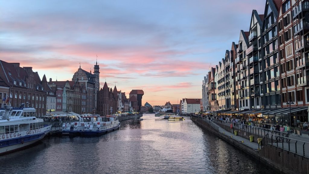 Quais et façades au bord de l’eau à Gdańsk Voie d’eau bordée de bâtiments historiques et contemporains, de quais et de bateaux sous un ciel de fin de journée