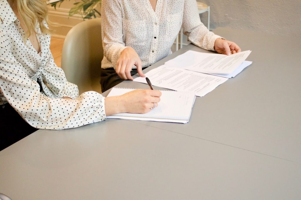 Relire les documents d’une société polonaise Deux personnes examinant des documents imprimés sur une table, l’une tenant un stylo et l’autre montrant une rubrique