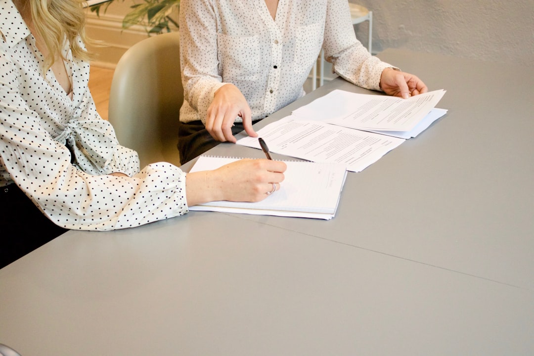 Deux personnes examinant des documents imprimés sur une table, l’une tenant un stylo et l’autre montrant une rubrique