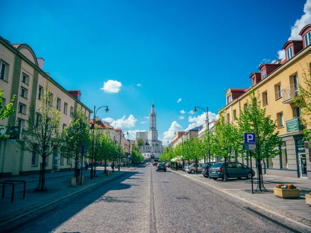 Rue commerçante pour un projet à Białystok Large rue piétonne bordée de façades claires, de lampadaires et d’arbres sous un ciel bleu