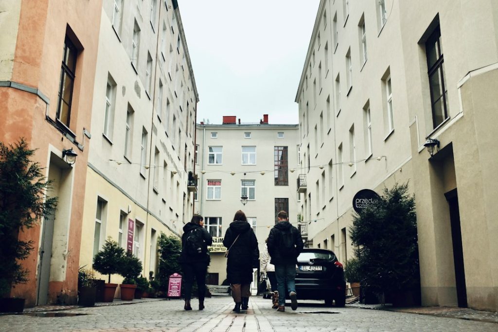 Passage entre de hauts immeubles clairs, avec des passants, une voiture et des façades ouvrant sur la rue